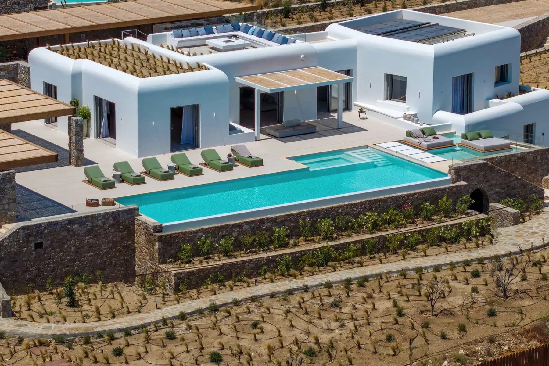 A modern white building overlooks a long outdoor swimming pool and sun loungers.