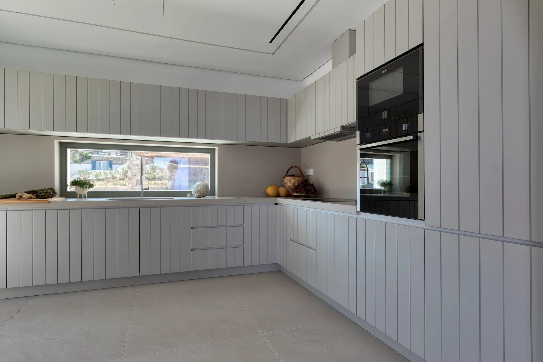 A modern kitchen with pale cabinetry, a wide window, and built-in appliances.
