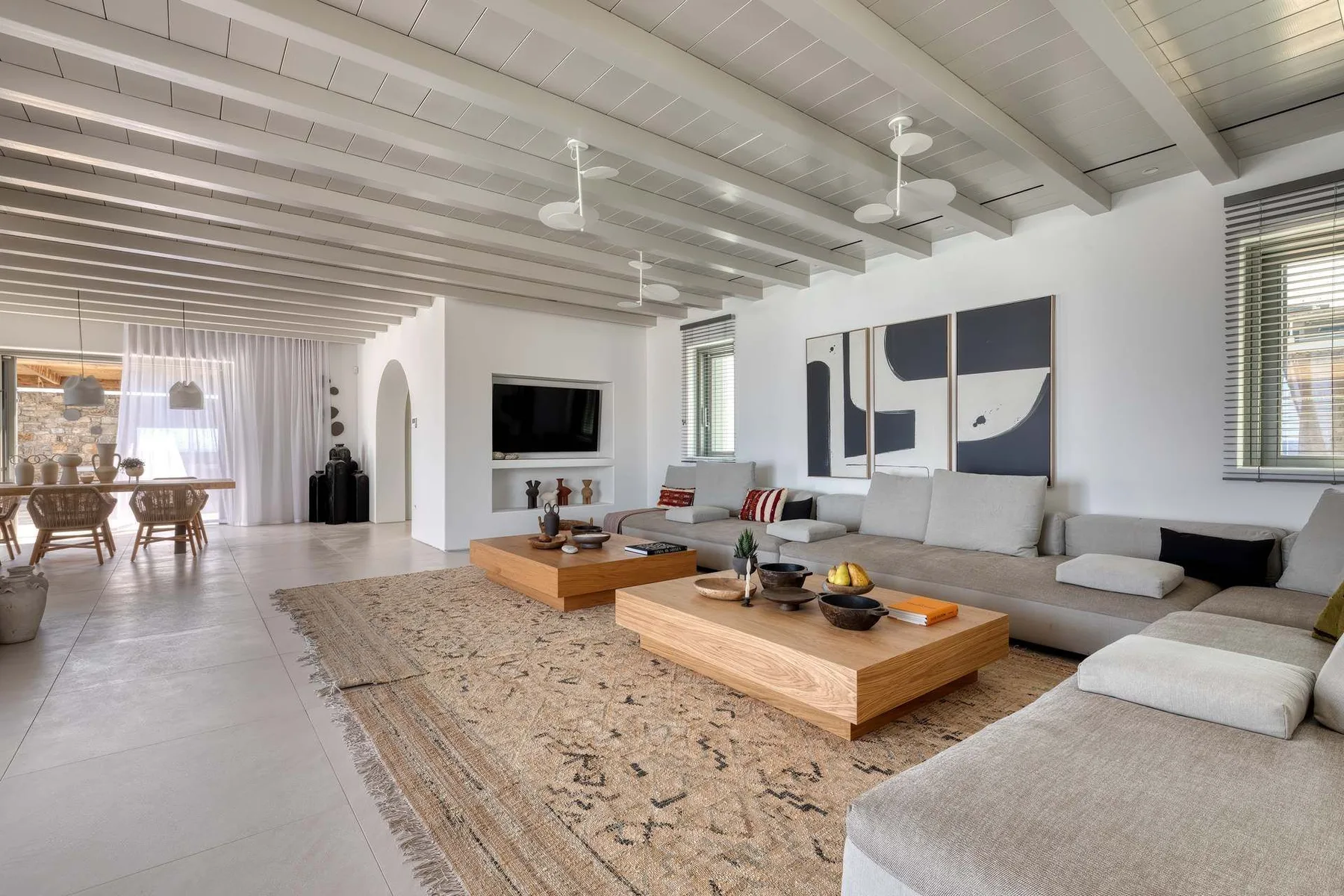 A bright living room with seating, low wooden tables, and a dining area beyond.