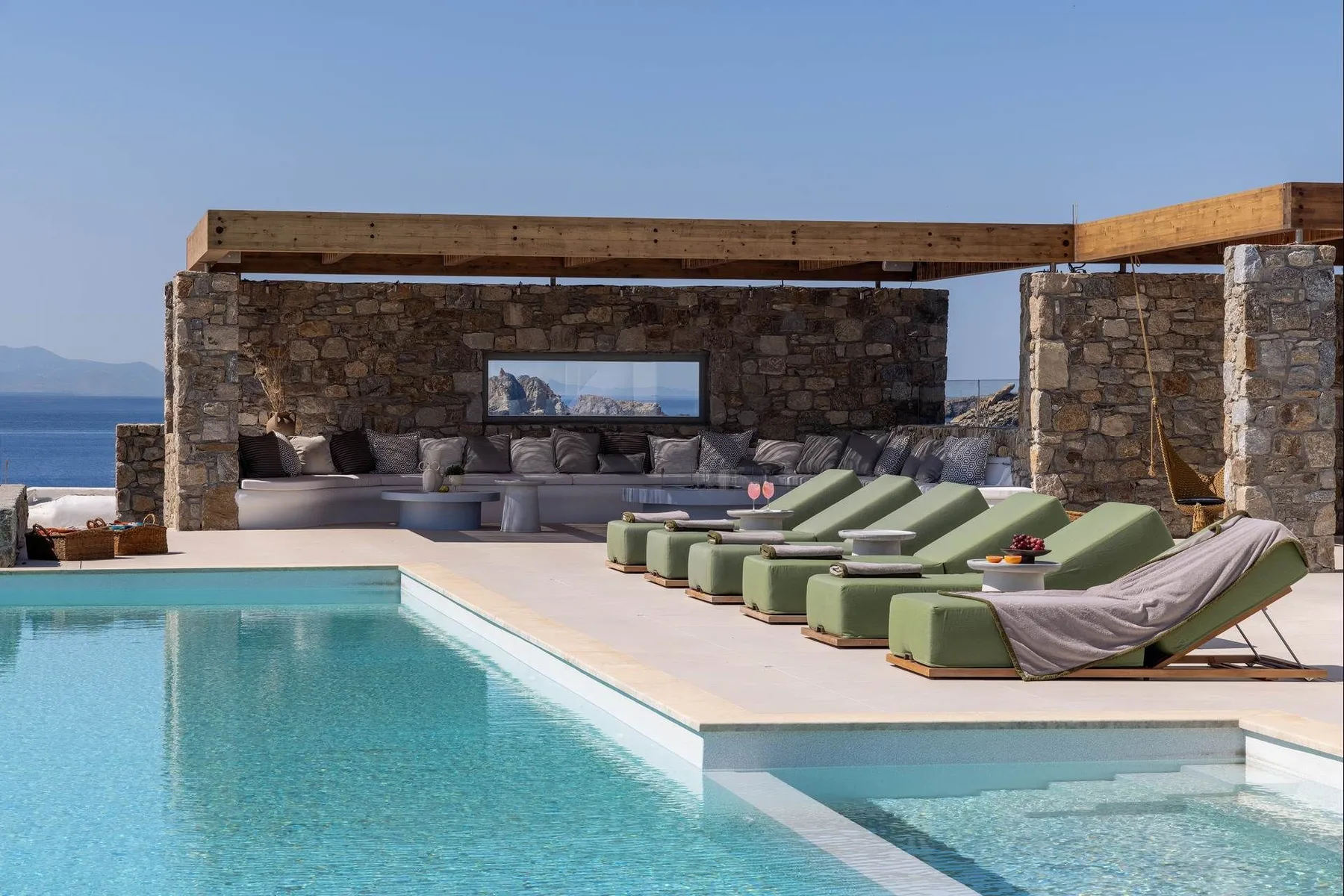 An outdoor pool beside a stone-walled lounge with cushioned seating.