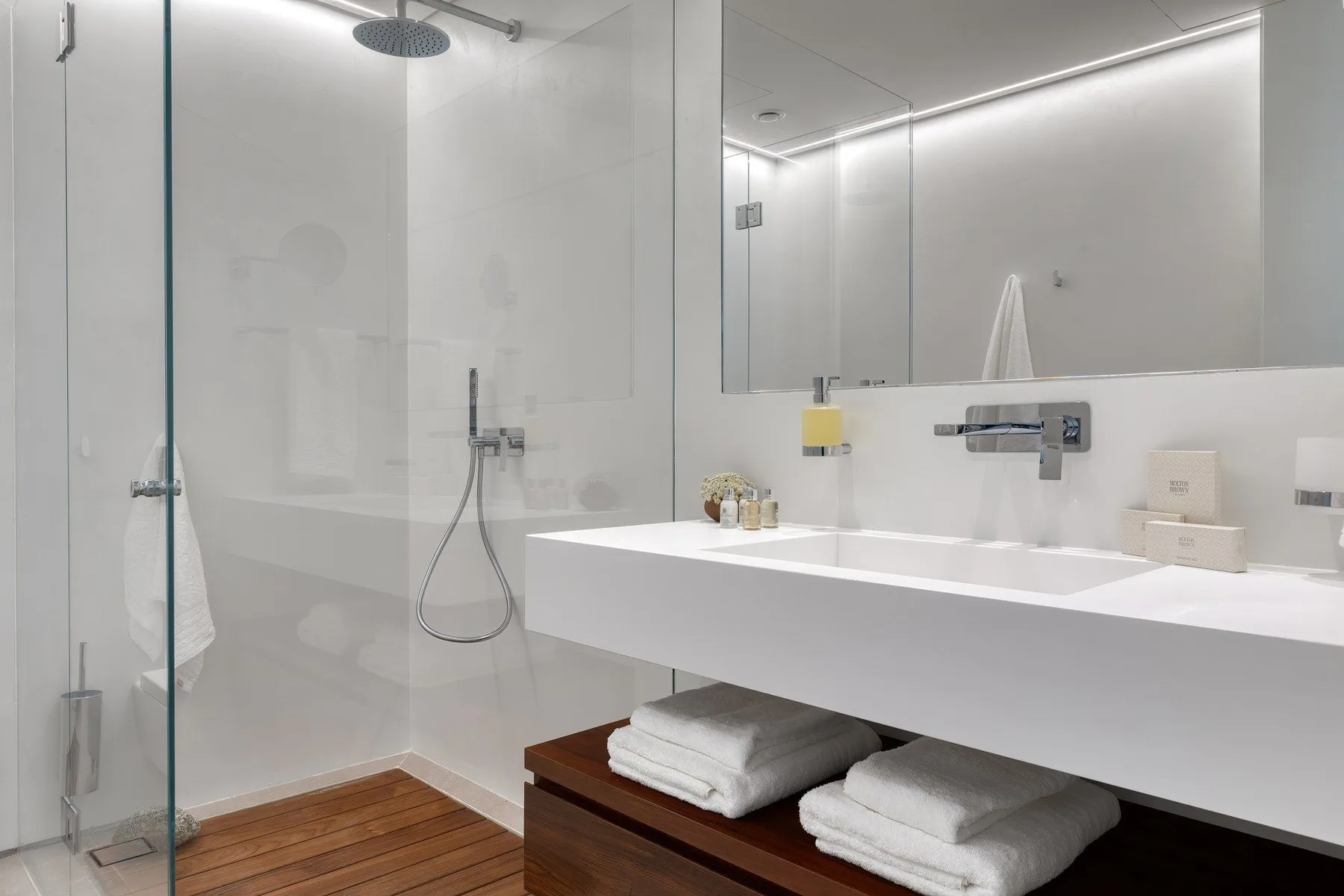 A modern bathroom with a glass shower and a long white vanity.