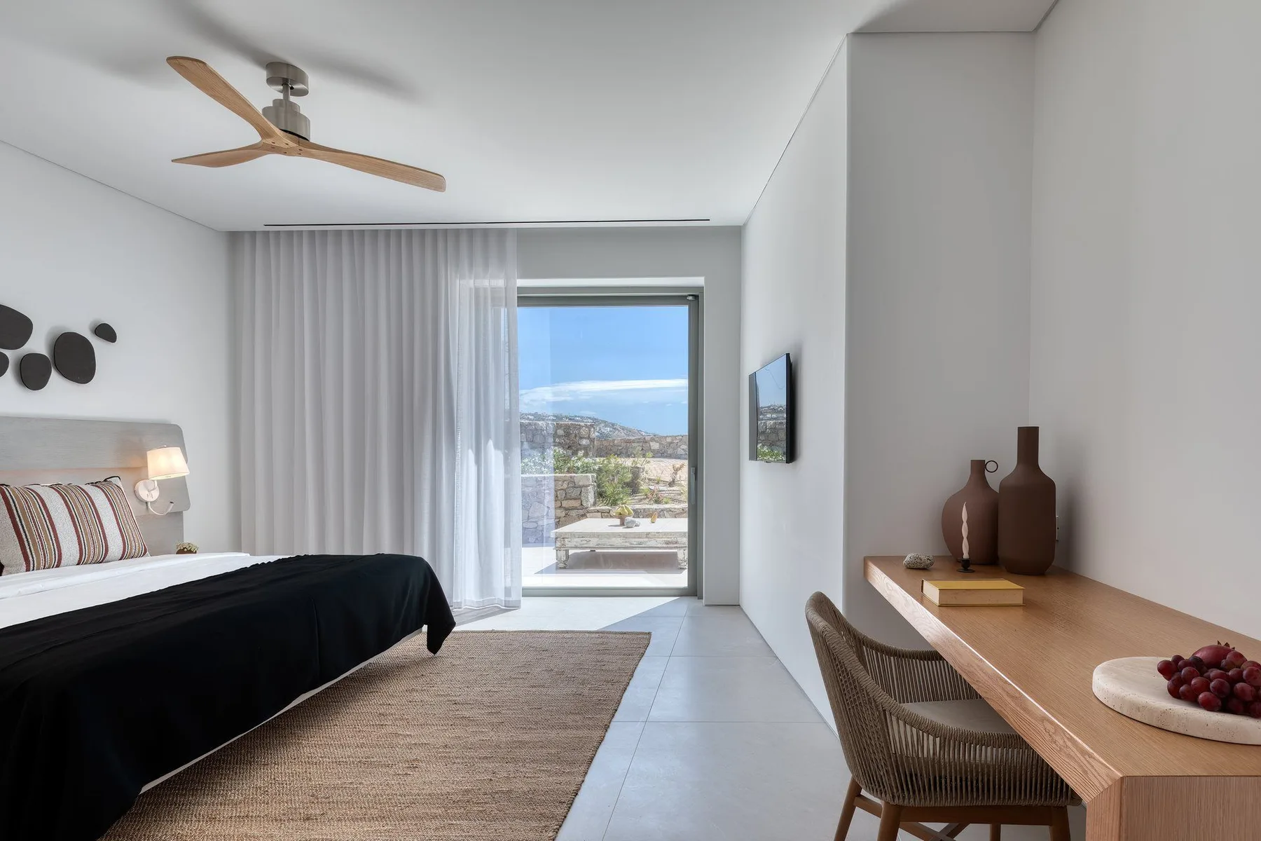A bright bedroom with a bed, desk, and sliding glass doors opening to a balcony.