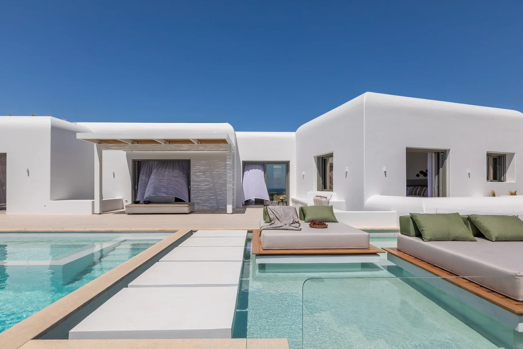 A modern white villa faces a swimming pool with cushioned outdoor seating.