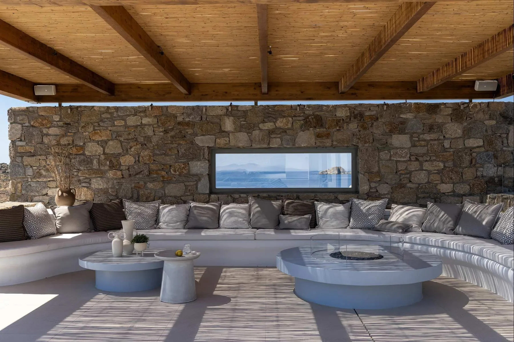 A covered outdoor lounge with curved seating and a stone wall overlooking the water.