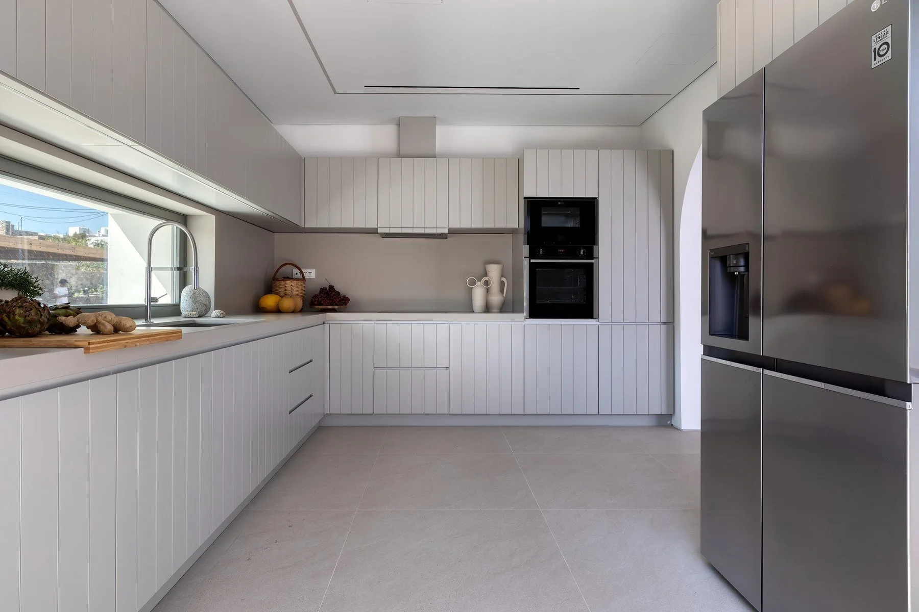 A modern kitchen with white cabinets, a wide window, and stainless steel appliances.