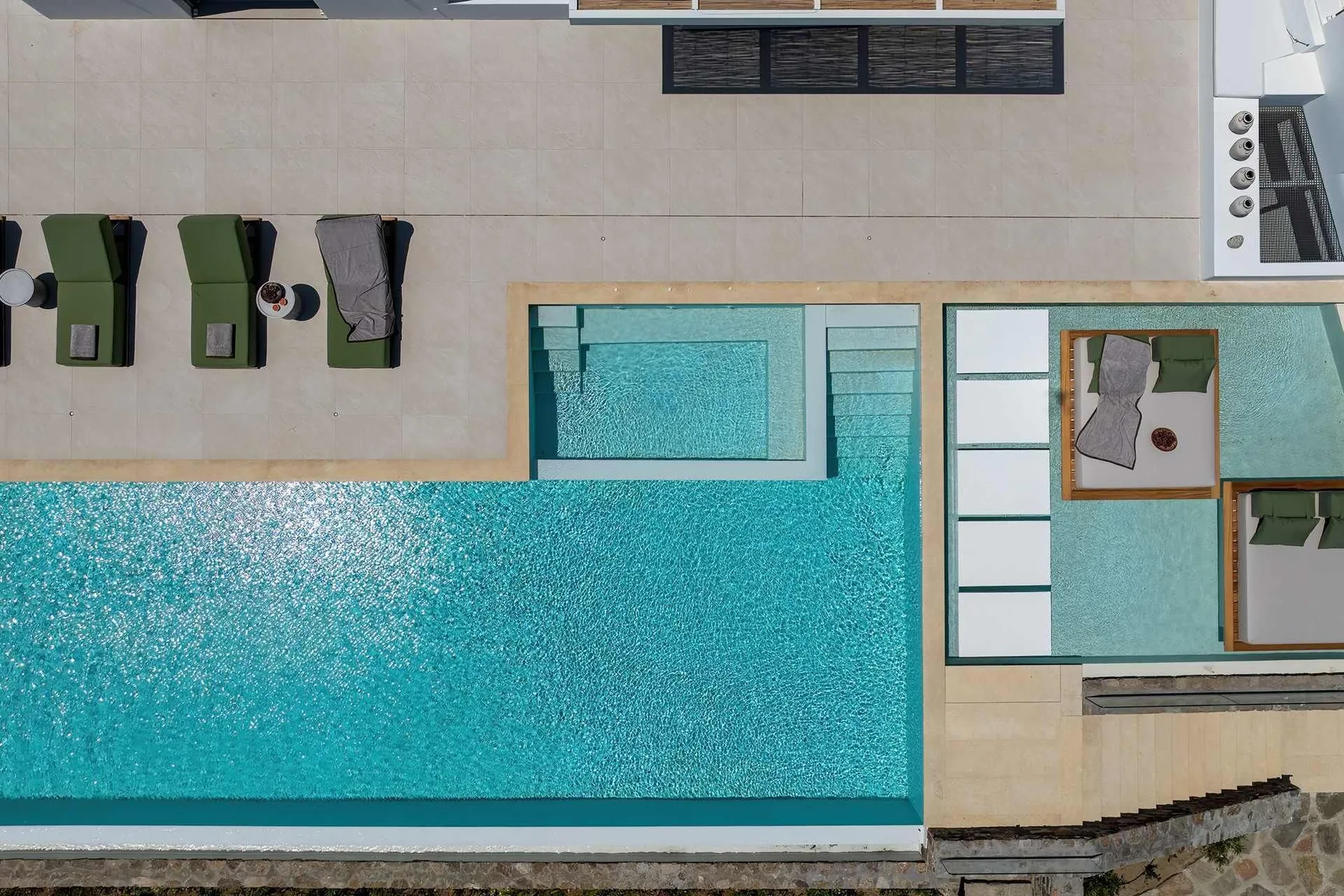 An overhead view of a swimming pool beside a paved deck with lounge seating.