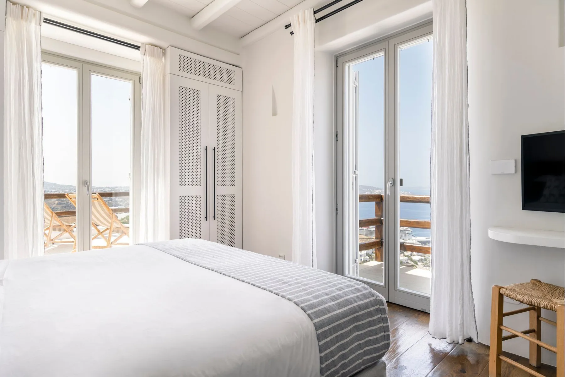 A bright bedroom with a bed beside tall glass doors opening onto a balcony.