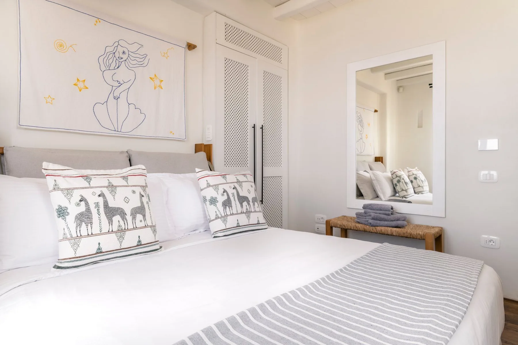 A bright bedroom with a neatly made bed and framed artwork above it.
