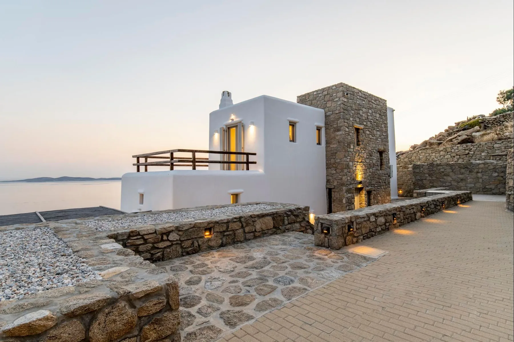 A white seaside building with stone walls and a paved terrace overlooks the water.