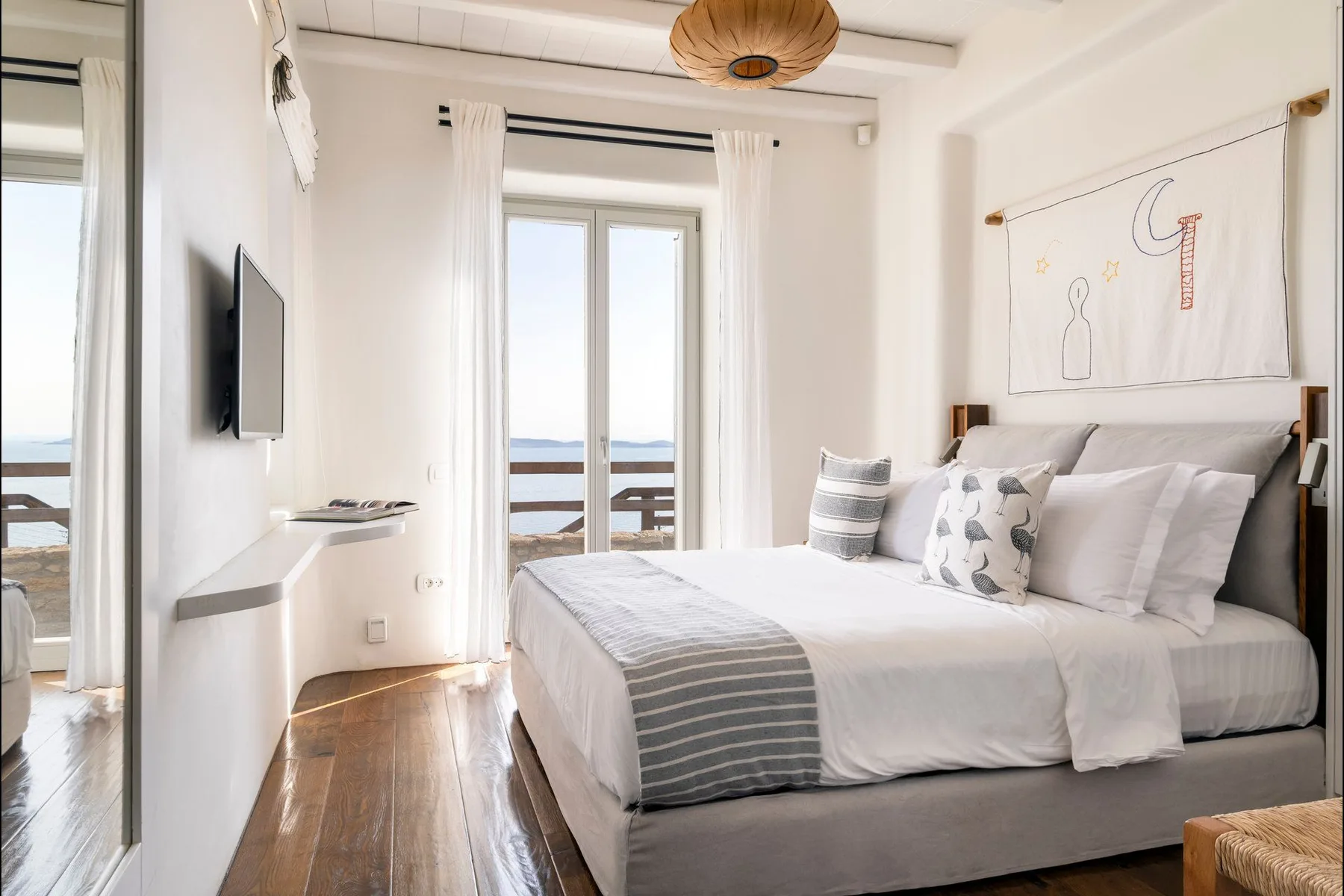 A bright bedroom with a neatly made bed beside glass doors opening to a balcony.