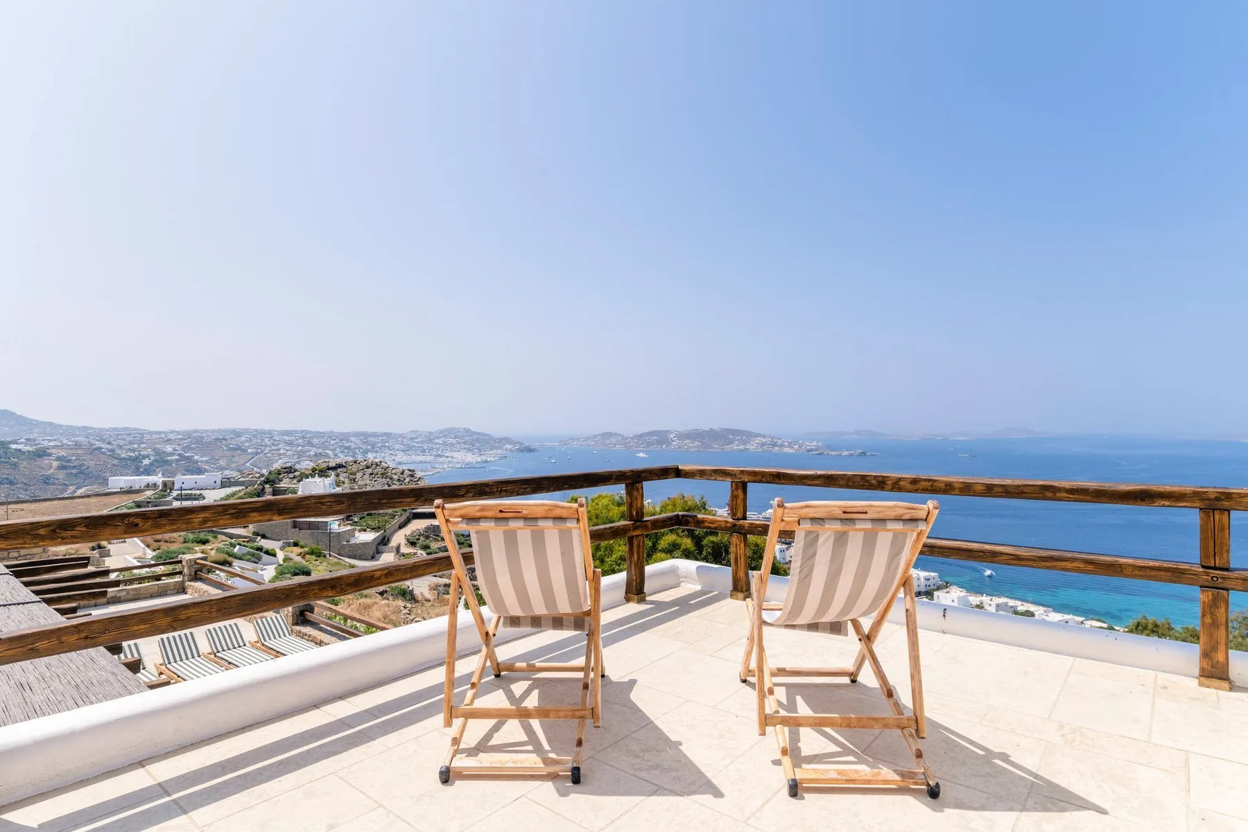 A rooftop terrace overlooks the sea, with two striped lounge chairs by the railing.