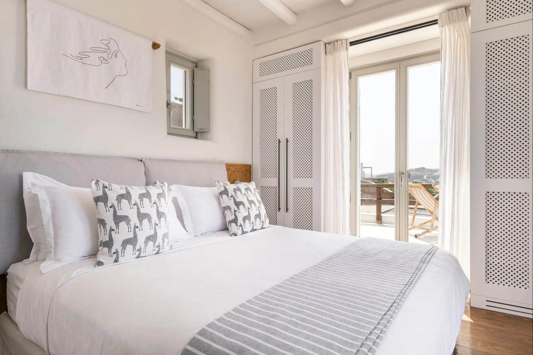A bright bedroom with a neatly made bed and tall windows.