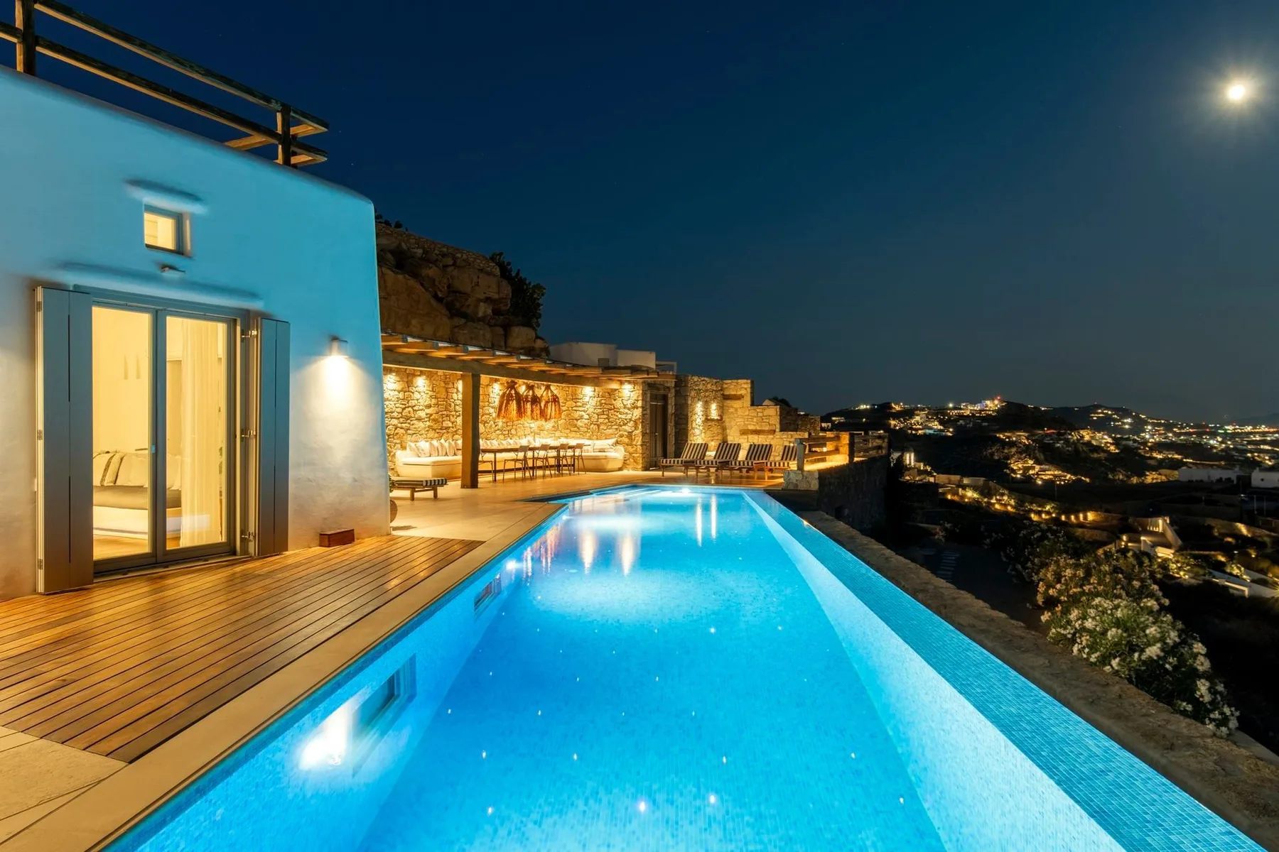 A brightly lit swimming pool beside a modern house at night.