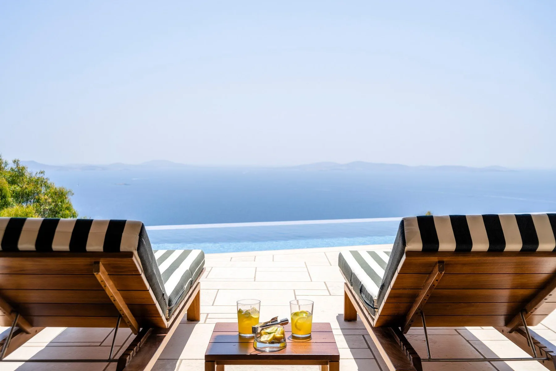 Two lounge chairs and a small table face a pool overlooking the water.