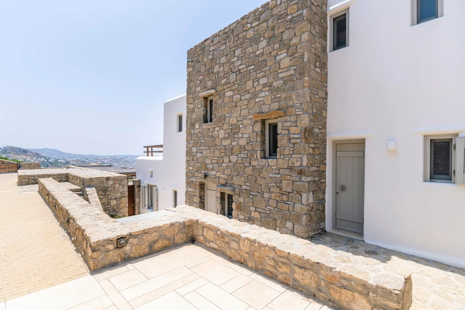 A stone terrace runs beside a white building, with distant hills visible.