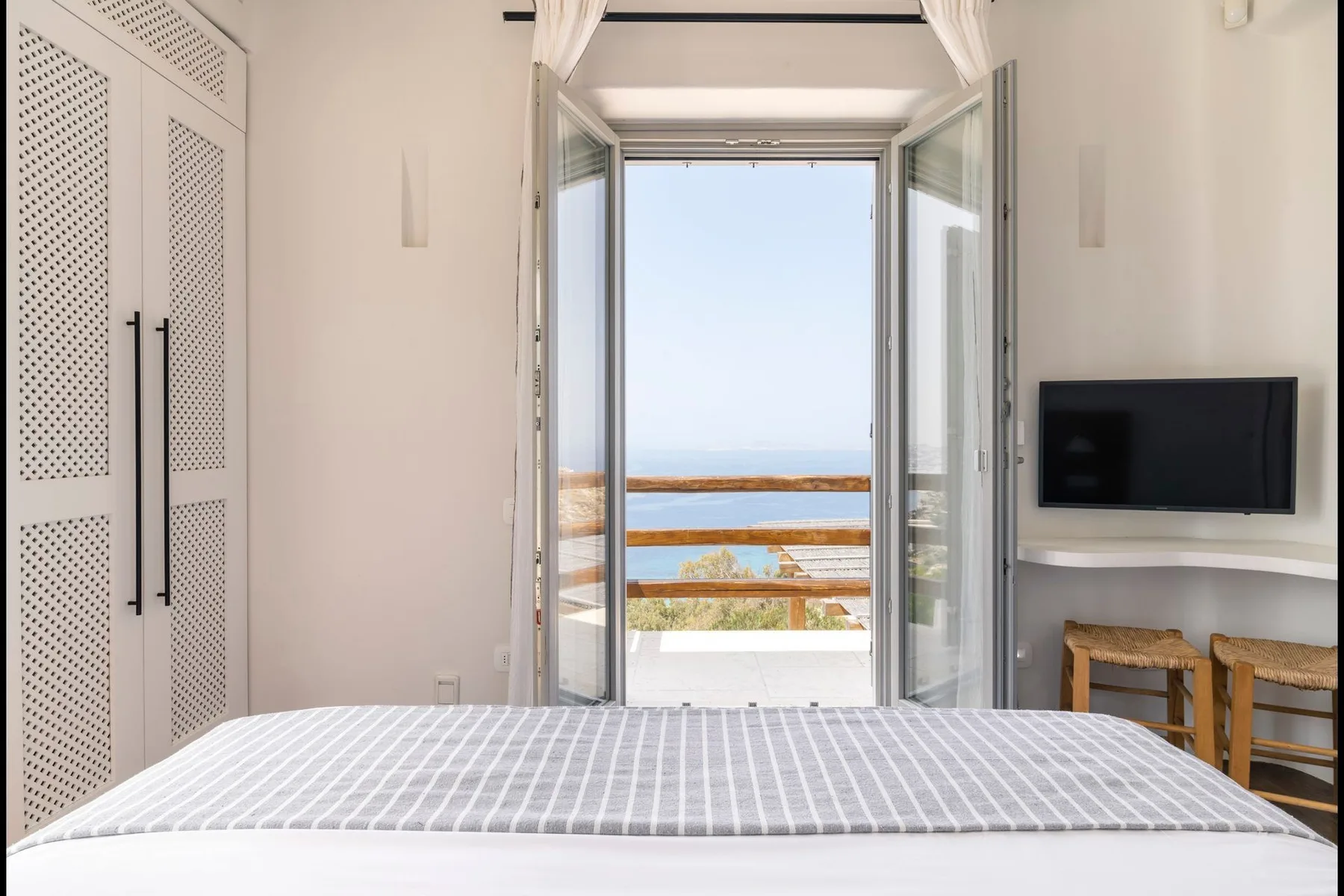 A bedroom with a bed facing open doors and a balcony overlooking the sea.