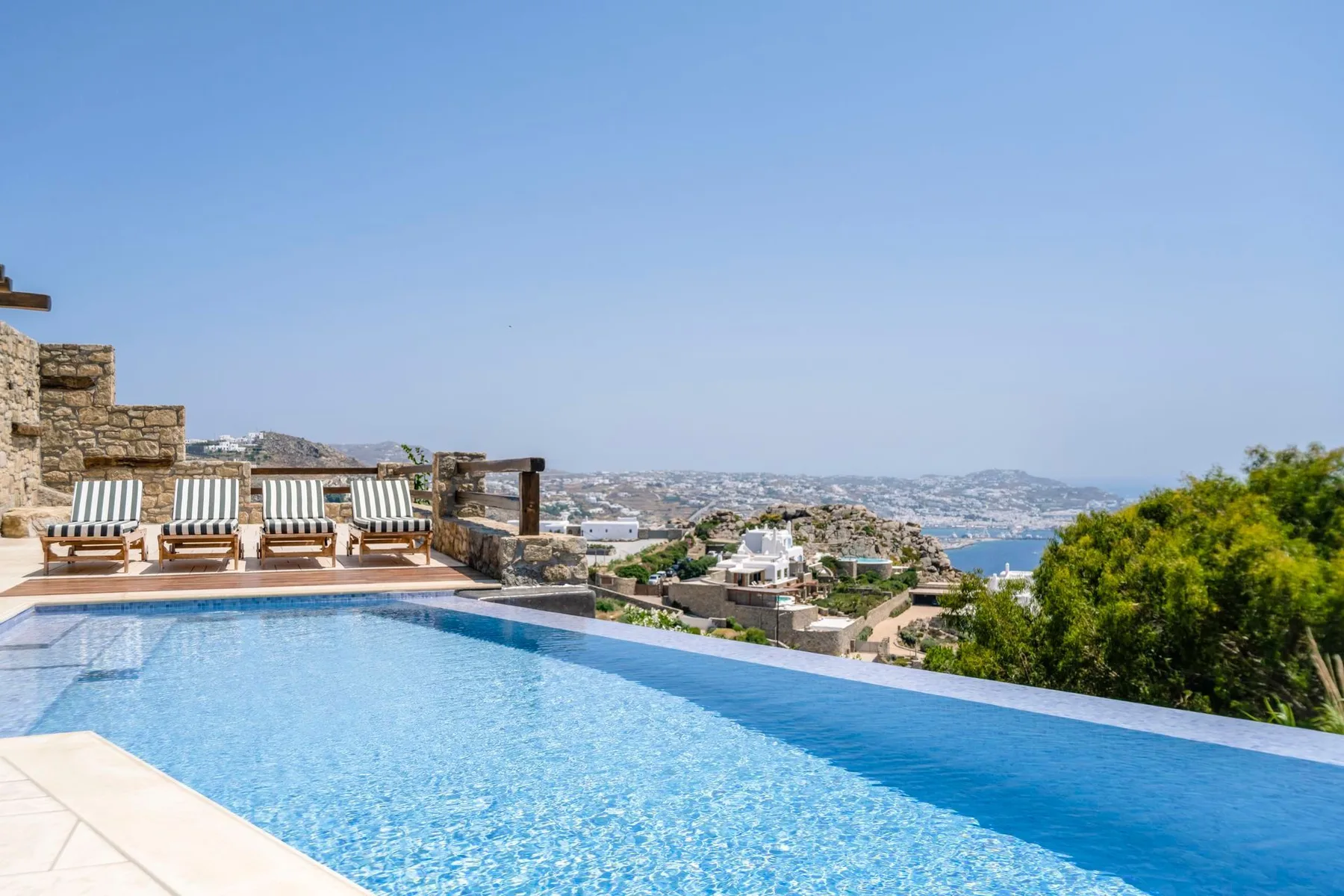 An outdoor swimming pool overlooks a coastal town and the sea.