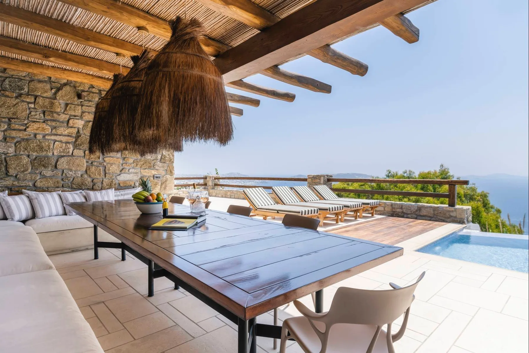 A shaded outdoor dining terrace beside a pool, with loungers along the railing.