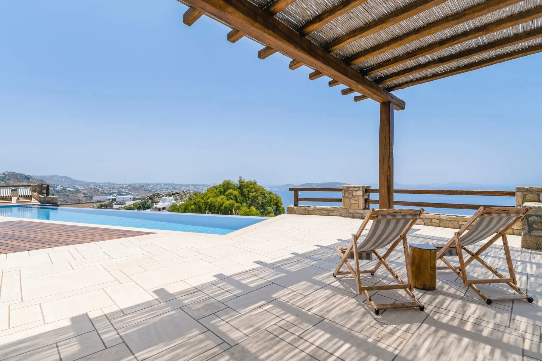A shaded terrace with lounge seating overlooks a swimming pool and distant landscape.