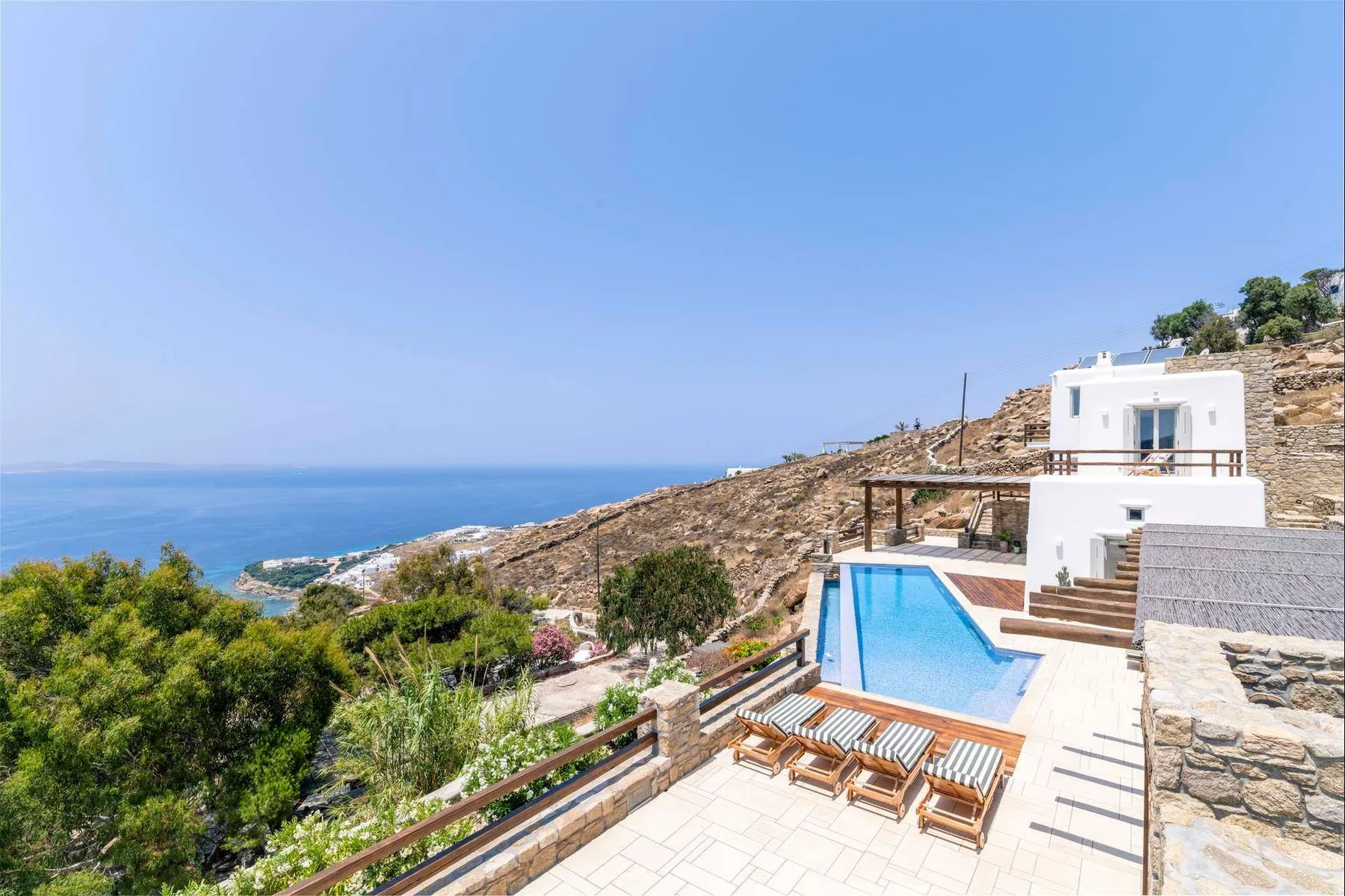 A hillside pool terrace overlooks the sea, with loungers beside the water.