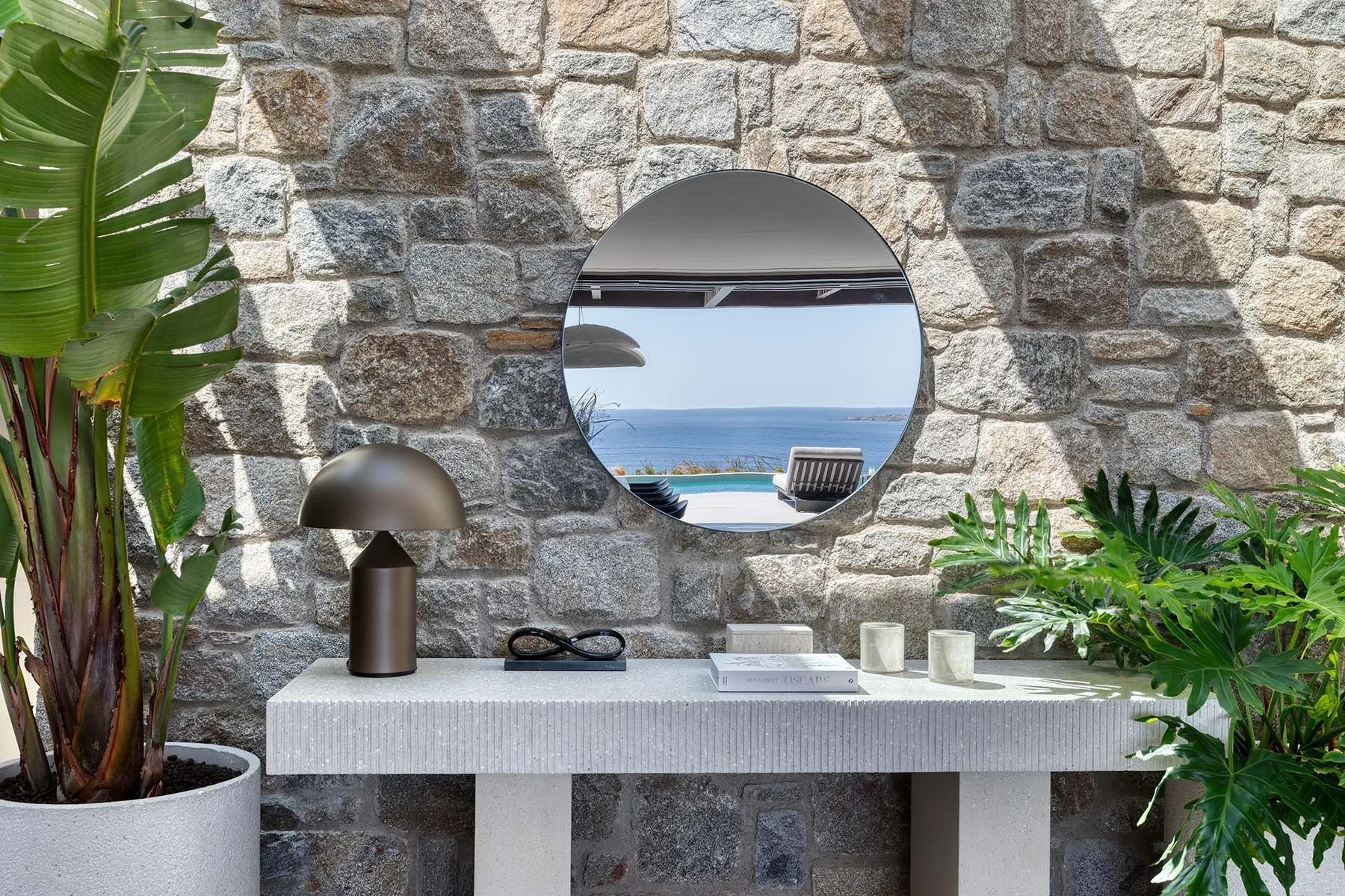 A bathroom vanity with a round mirror is set against a stone wall.