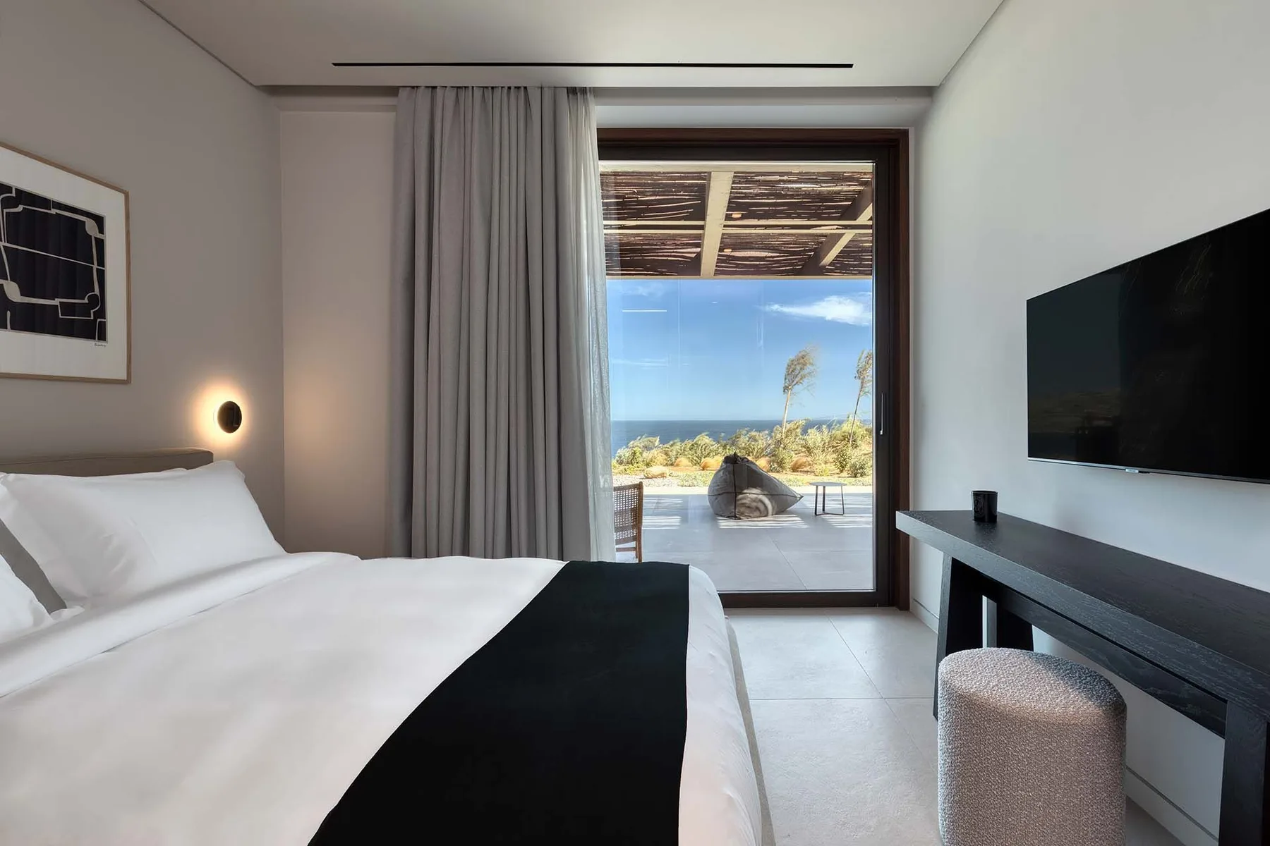 A bedroom with a bed, a desk, and glass doors opening onto a terrace.