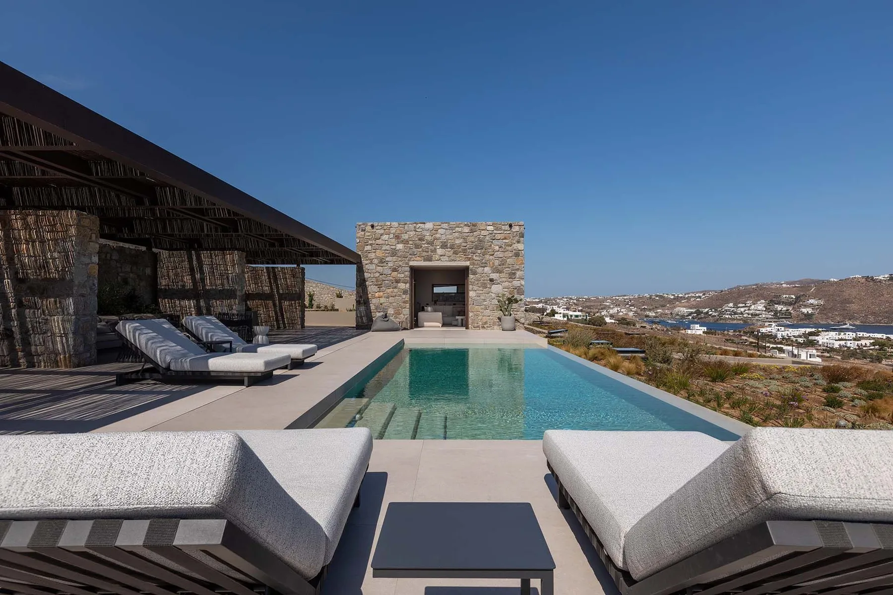 An outdoor swimming pool with lounge seating overlooks a dry, built-up landscape.