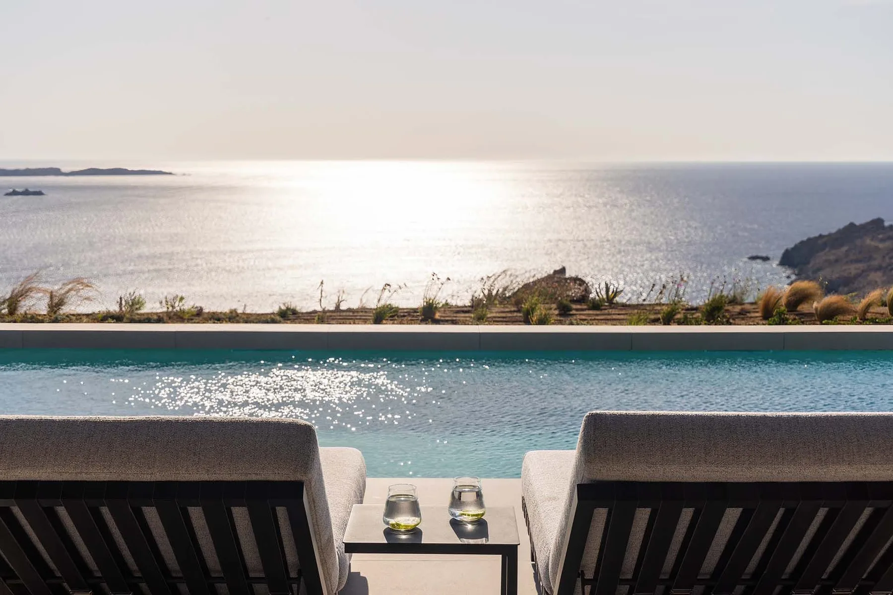 Two lounge chairs face a swimming pool and the sea.