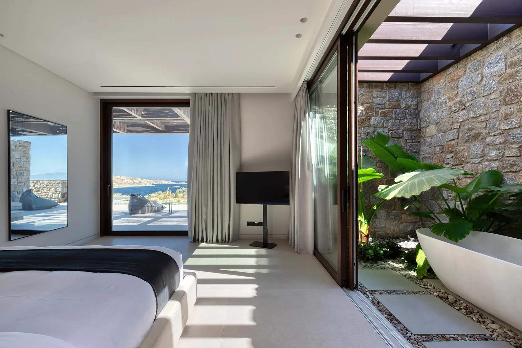 A bright bedroom opens onto a small stone-walled courtyard with leafy plants.