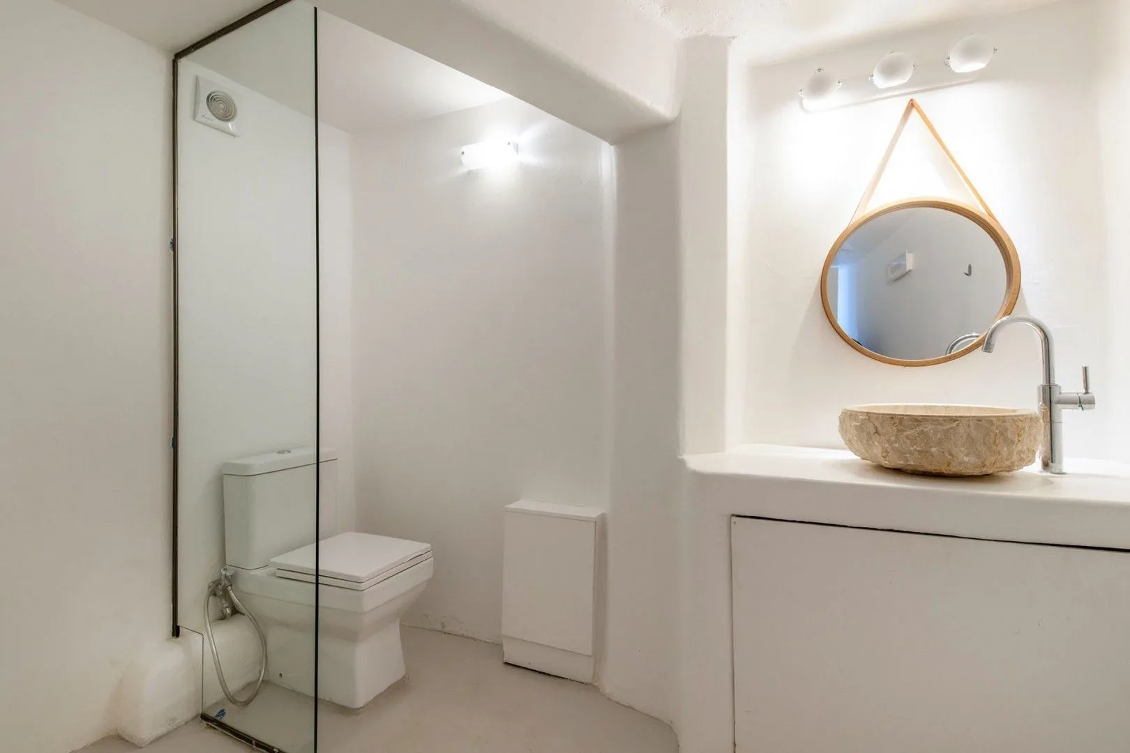 A bright bathroom with a glass shower partition, toilet, and stone basin.