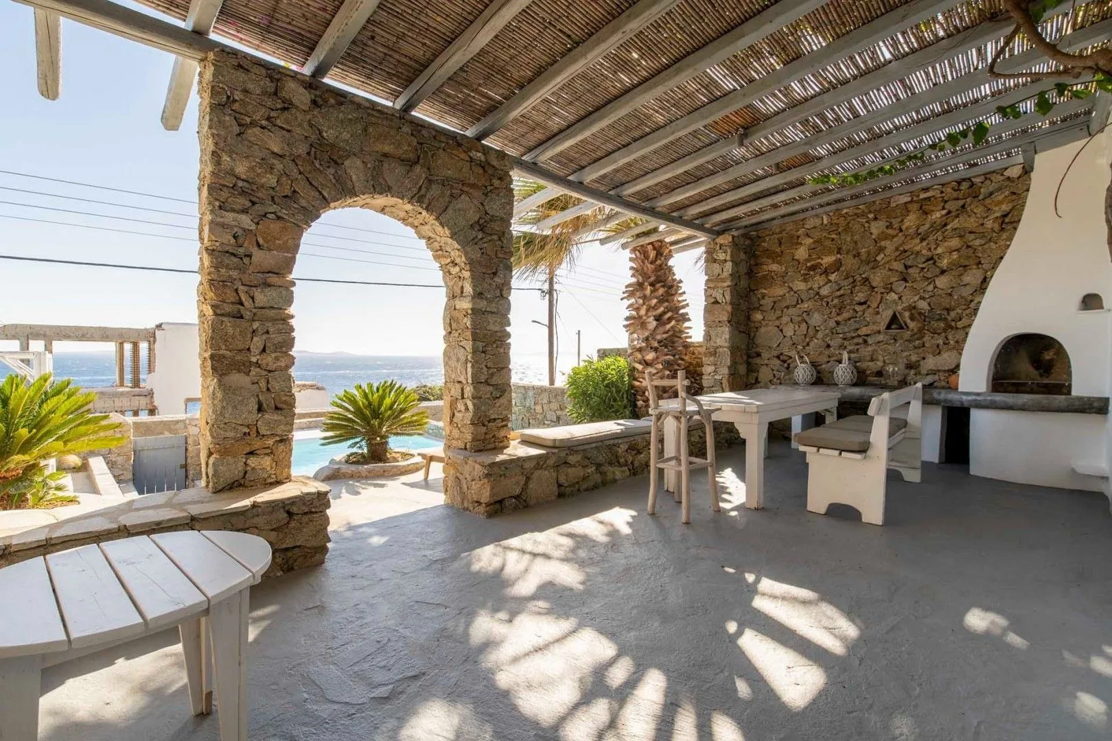 A covered stone patio has an outdoor dining table and a built-in oven.