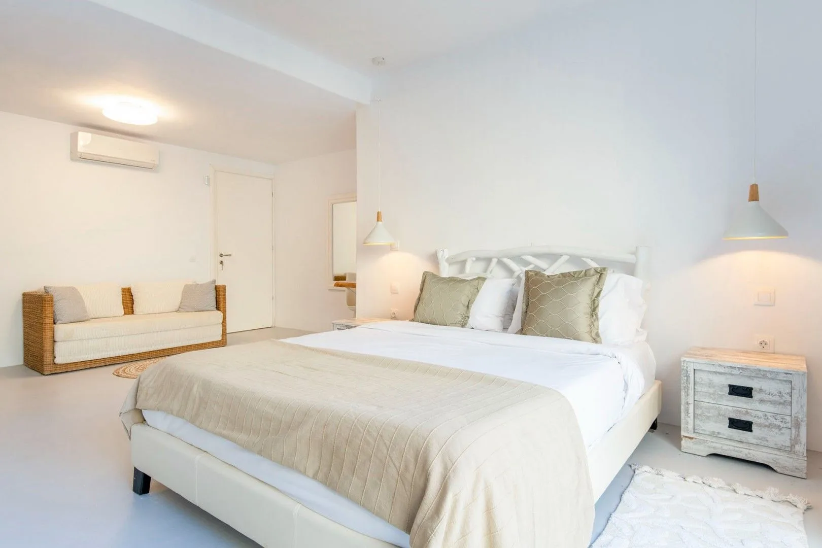 A bright bedroom with a large bed and a small sofa along the wall.