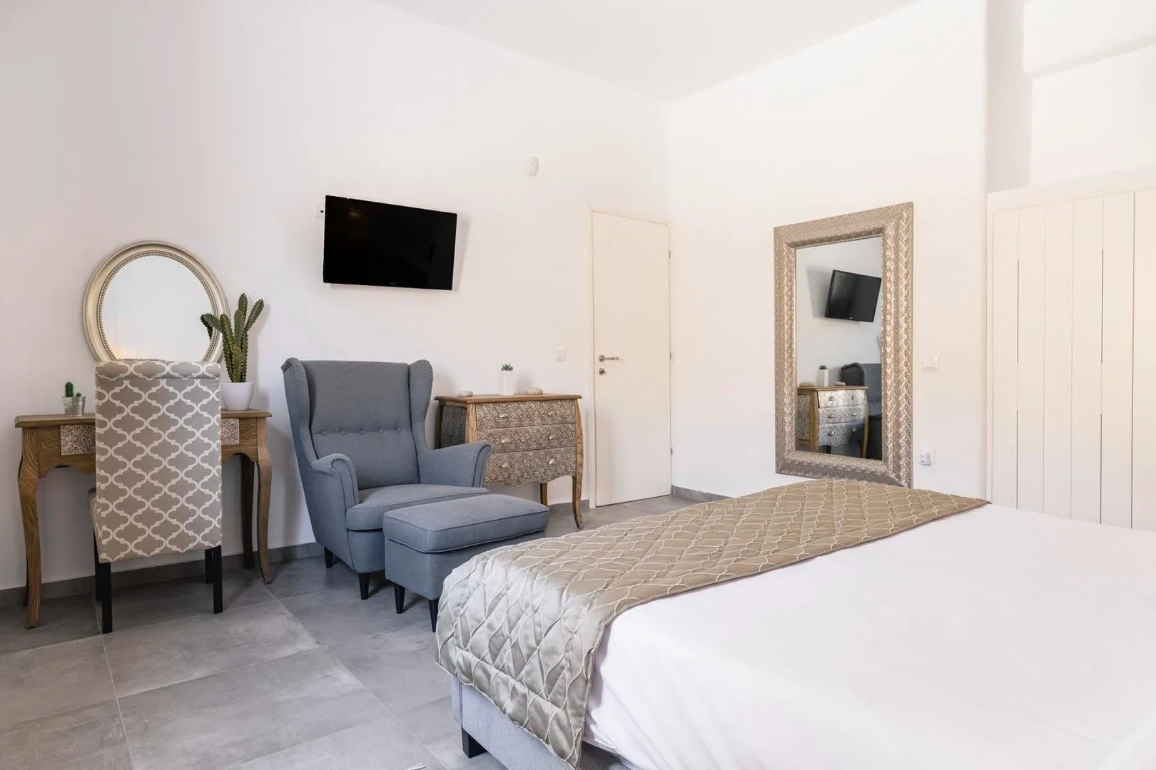 A bedroom with a bed, a blue armchair, and a wall-mounted television.