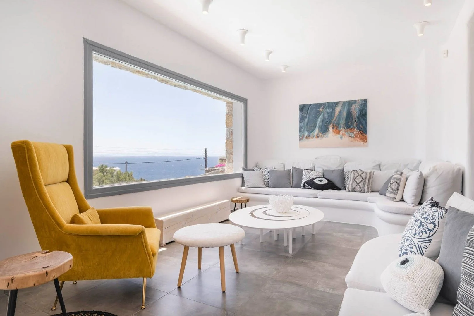 A bright living room with seating arranged around a round coffee table beside a large window.