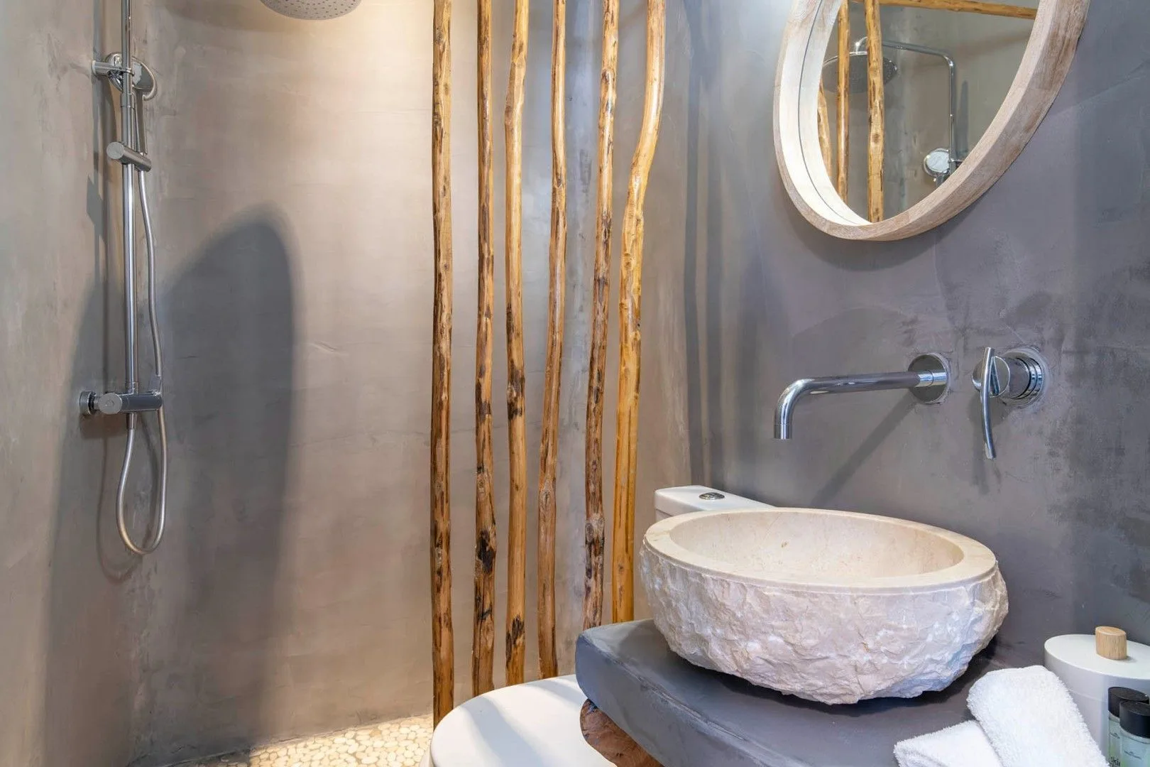 A bathroom with a stone basin, wall-mounted faucet, and shower.