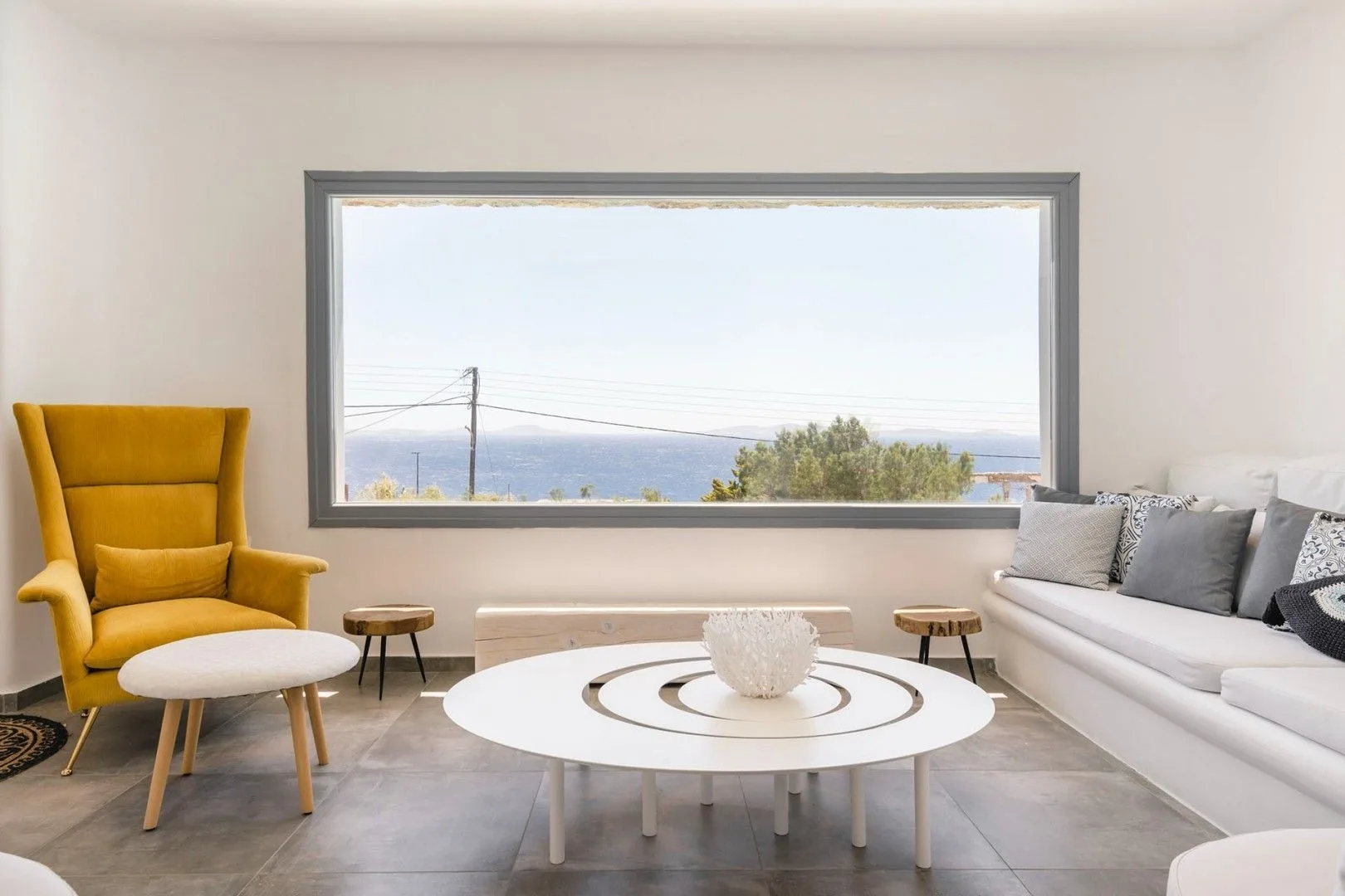 A bright living room with a white sofa and a large window overlooking the water.