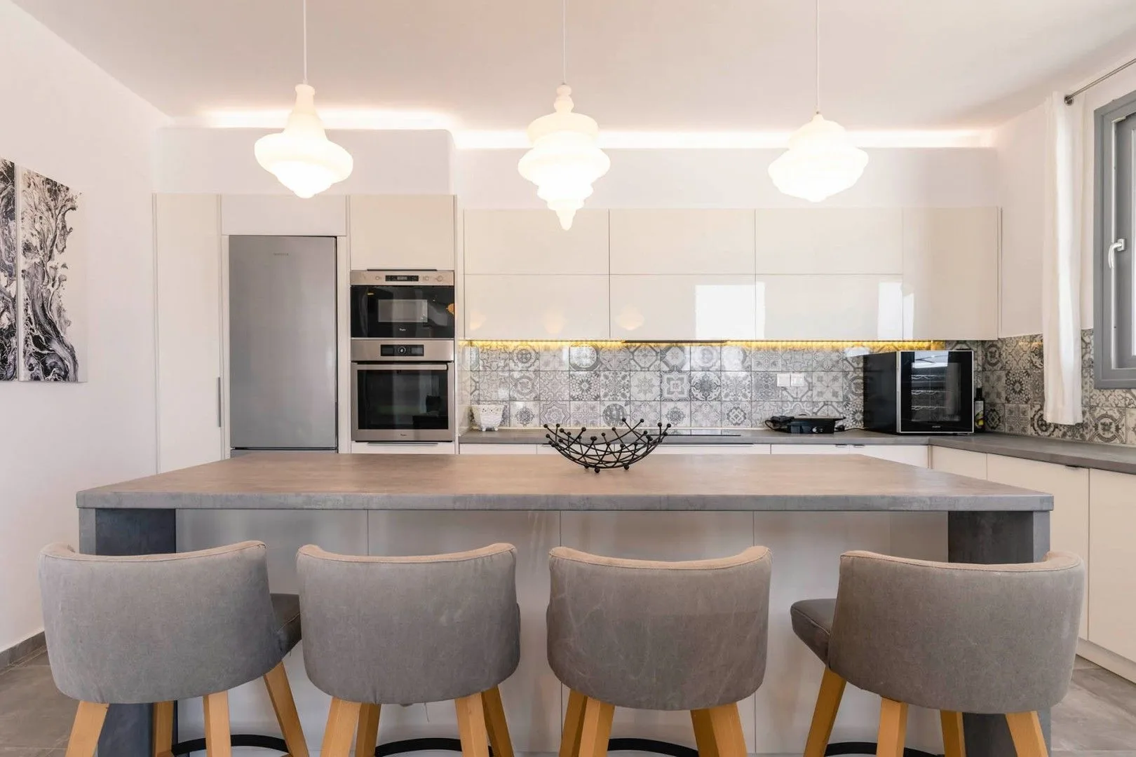 A bright kitchen with a wide island and gray upholstered seating.