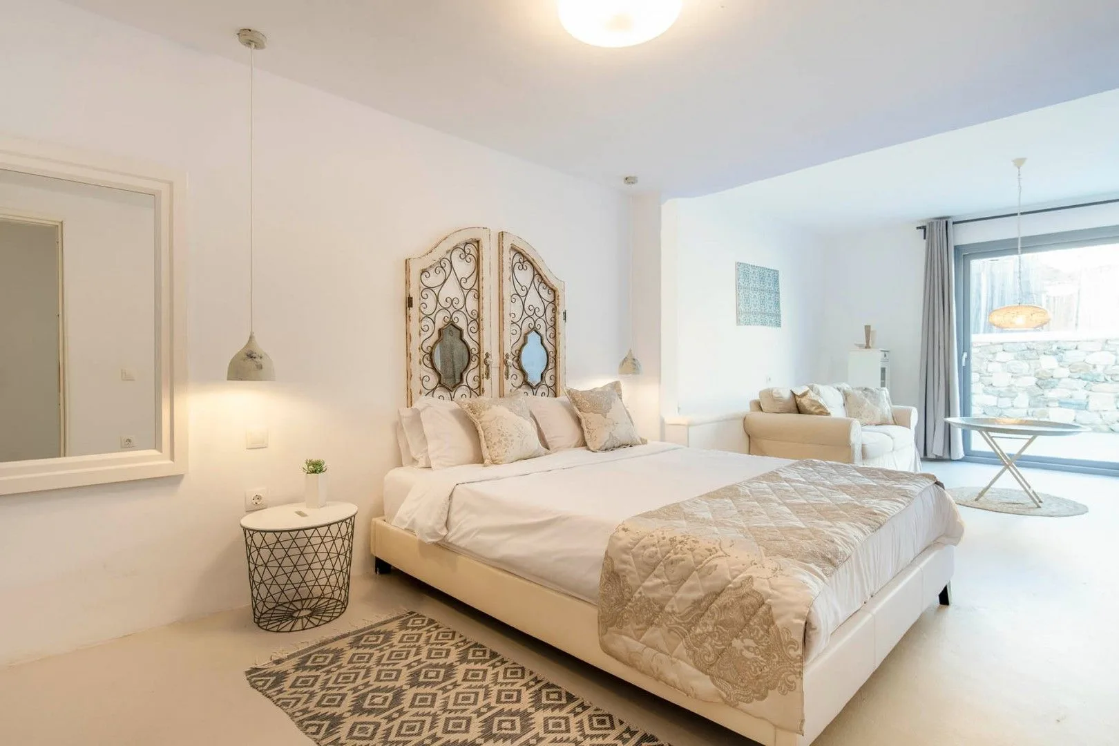 A bright bedroom with a large bed and a window overlooking a stone wall.