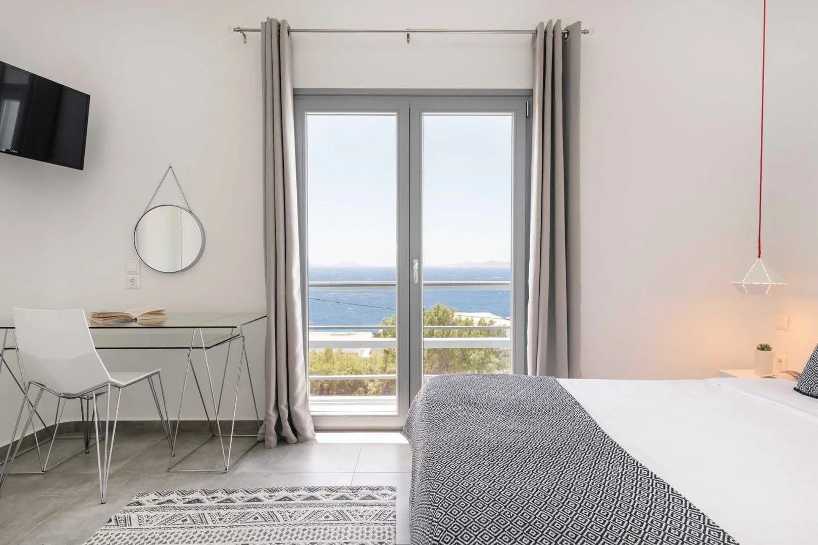 A bright bedroom with a bed beside glass doors opening onto a sea view.