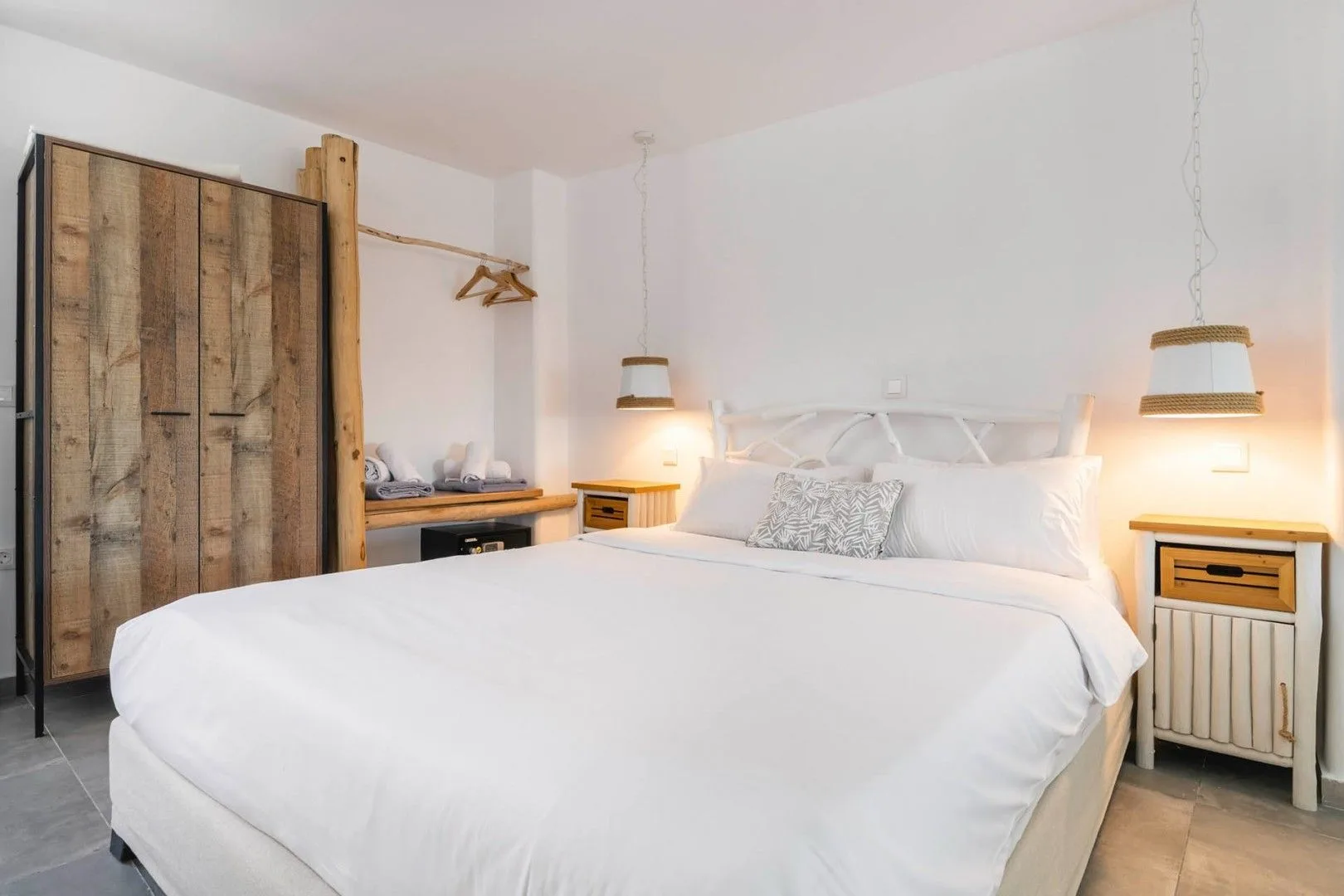 A bright bedroom with a large bed, bedside tables, and a wooden wardrobe.