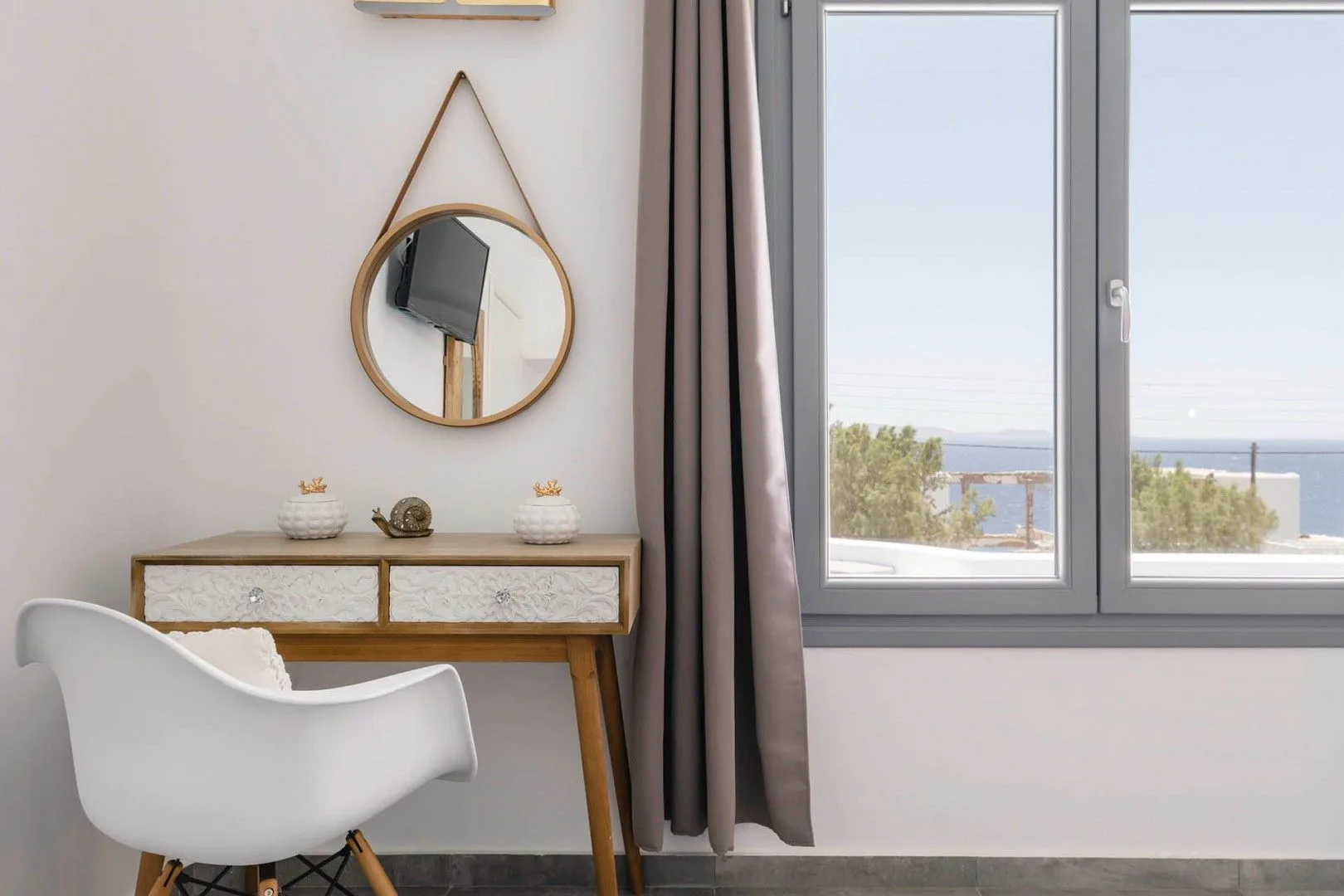 A small desk and chair sit beside a window overlooking the sea.