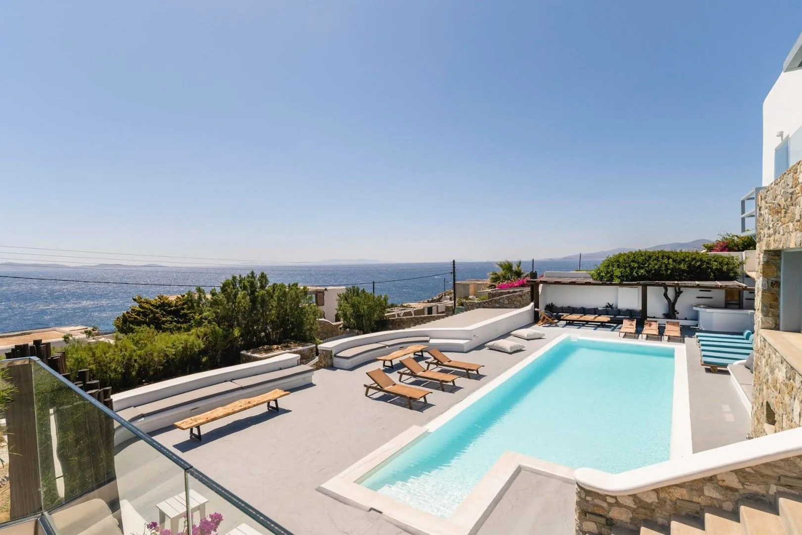 A pool terrace overlooks the sea, with lounge chairs arranged beside the water.