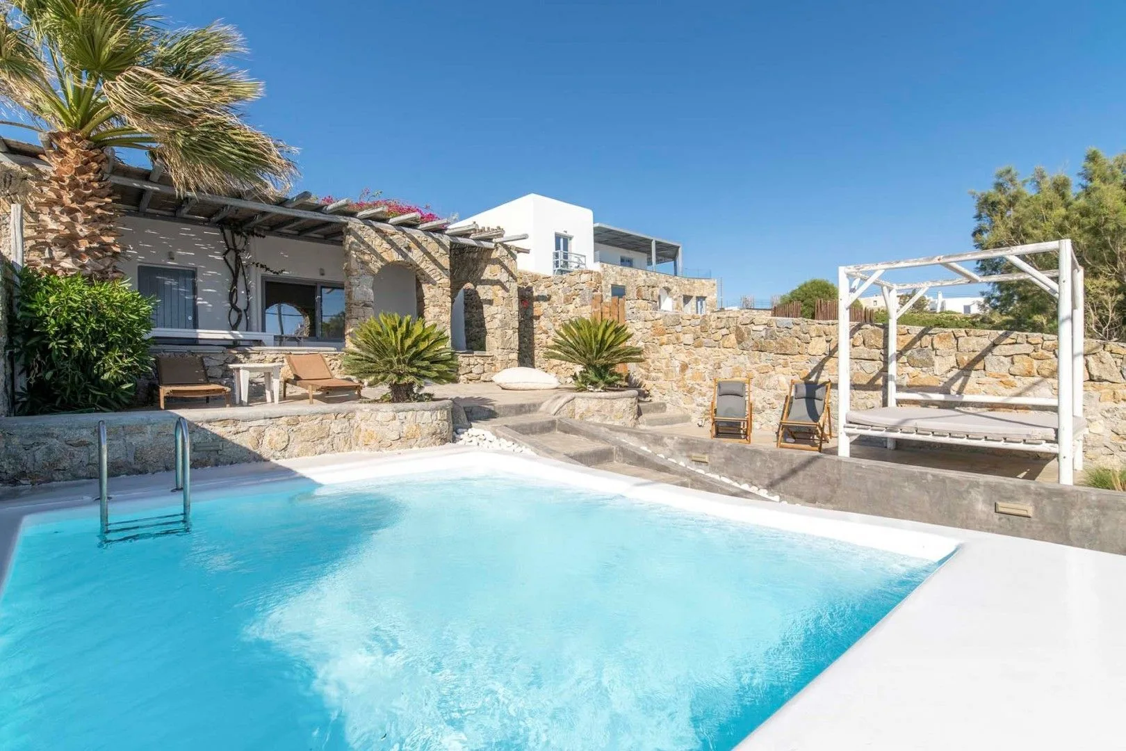 An outdoor swimming pool beside a stone terrace and a white canopy bed.