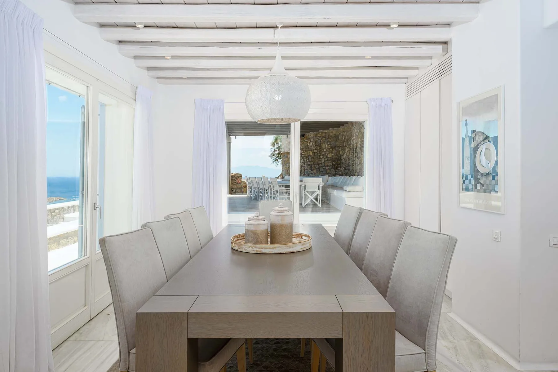 A bright dining area with a long table and views of the sea.