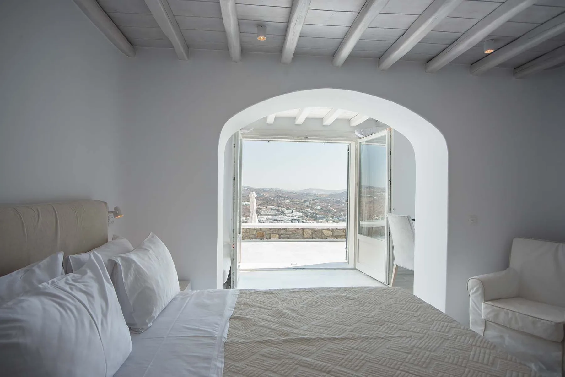 A bright bedroom with a bed beside open doors leading to a balcony.