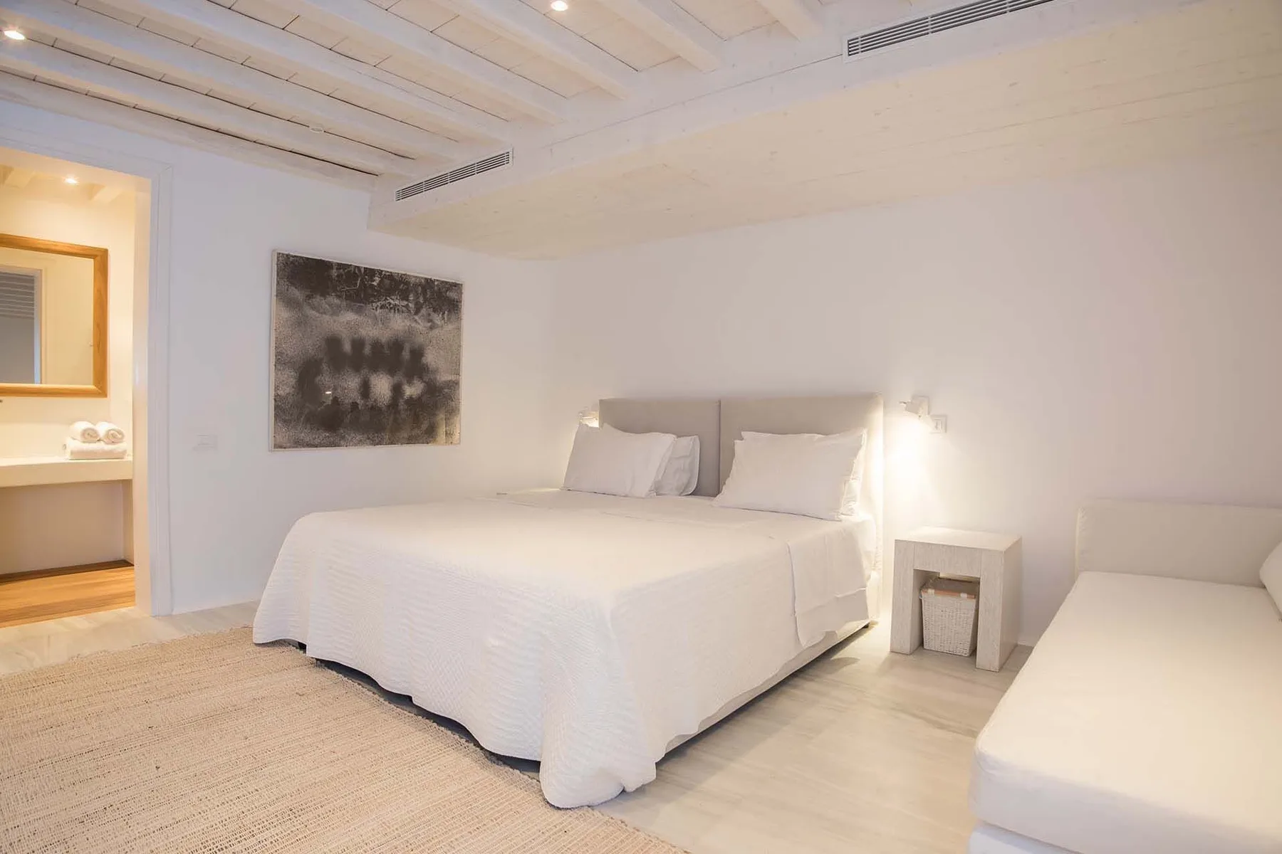 A bright bedroom with a large bed, bedside table, and wall art.
