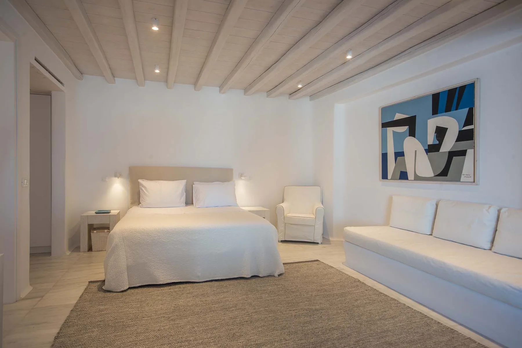 A bedroom with a neatly made bed and a sofa beneath abstract wall art.
