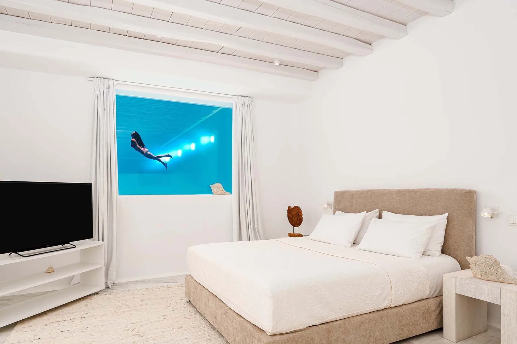 A bright bedroom with a large bed beside a window overlooking the sea.