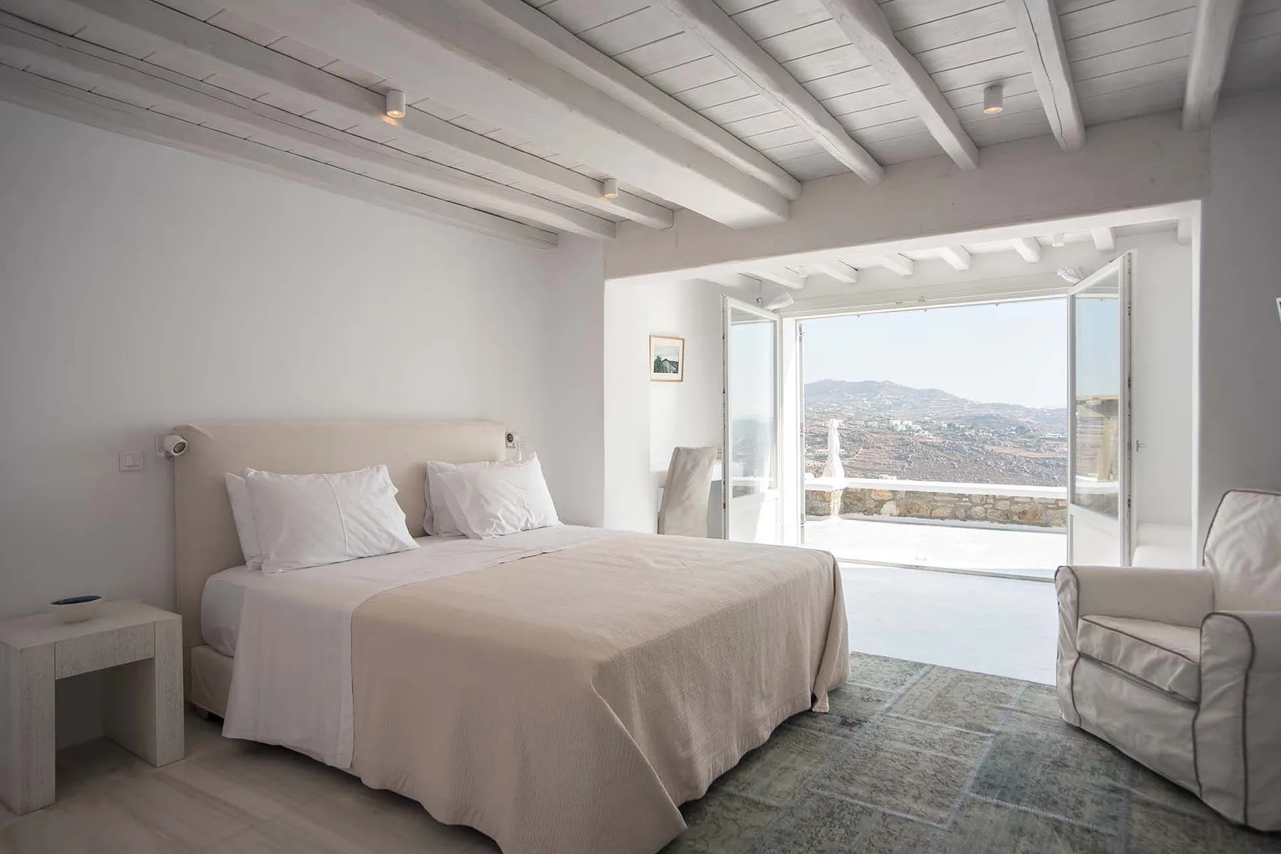 A bright bedroom with a double bed and open doors leading to a terrace.