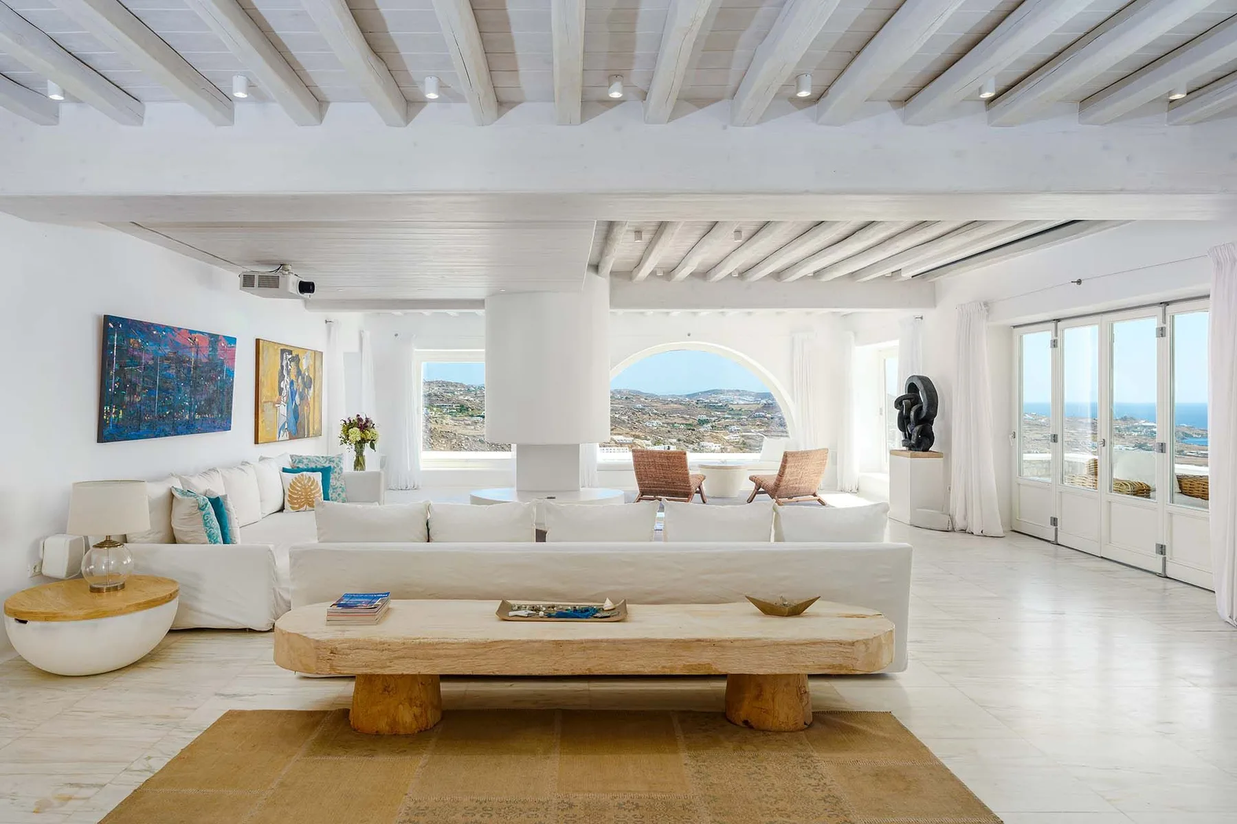 A bright living room with white seating and large windows overlooking the sea.